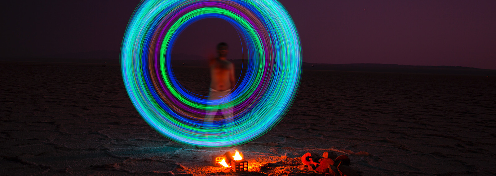 image of an illuminated circle above a camp fire and in front of a figure