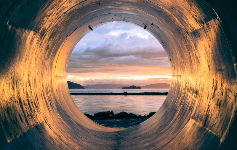 Image looking out at a waterscape through a circular tunnel