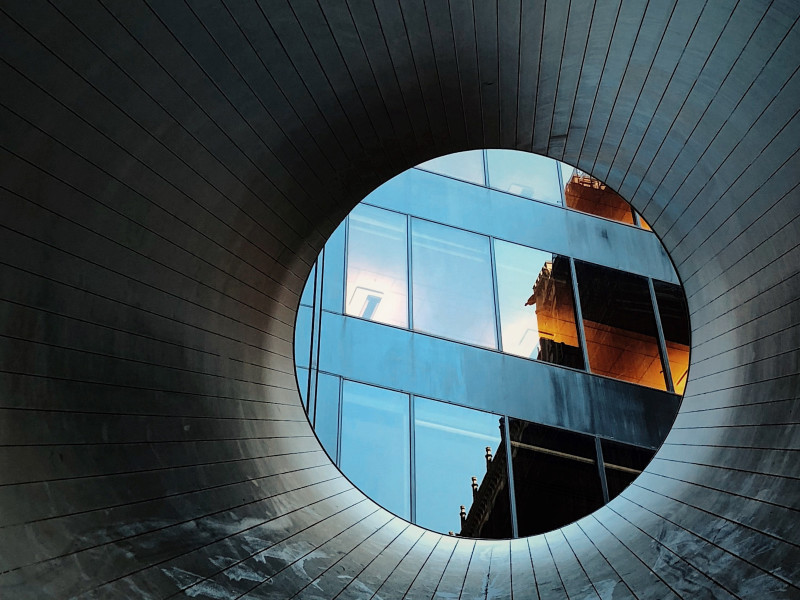 Image looking through a circular tunnel to a corporate building scene