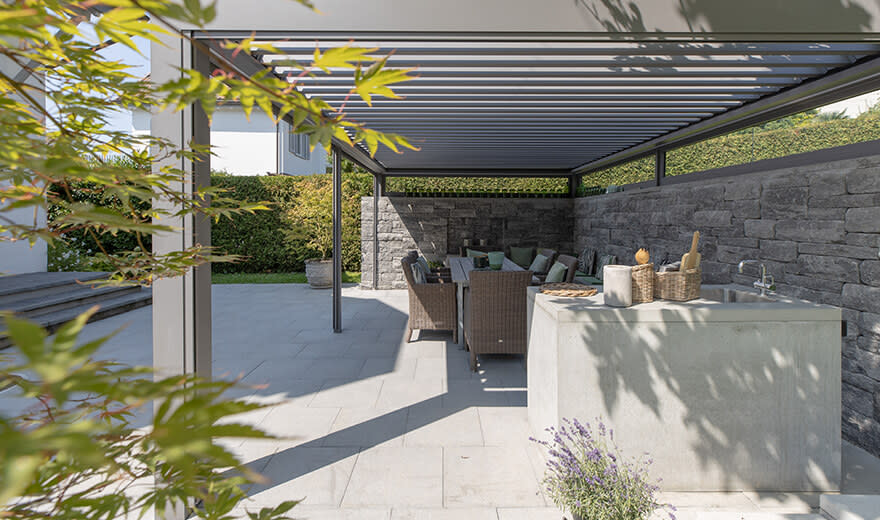 outdoorküche Aussicht auf eine Pergola unter welcher eine Outdoorküche steht und eine Lounge.