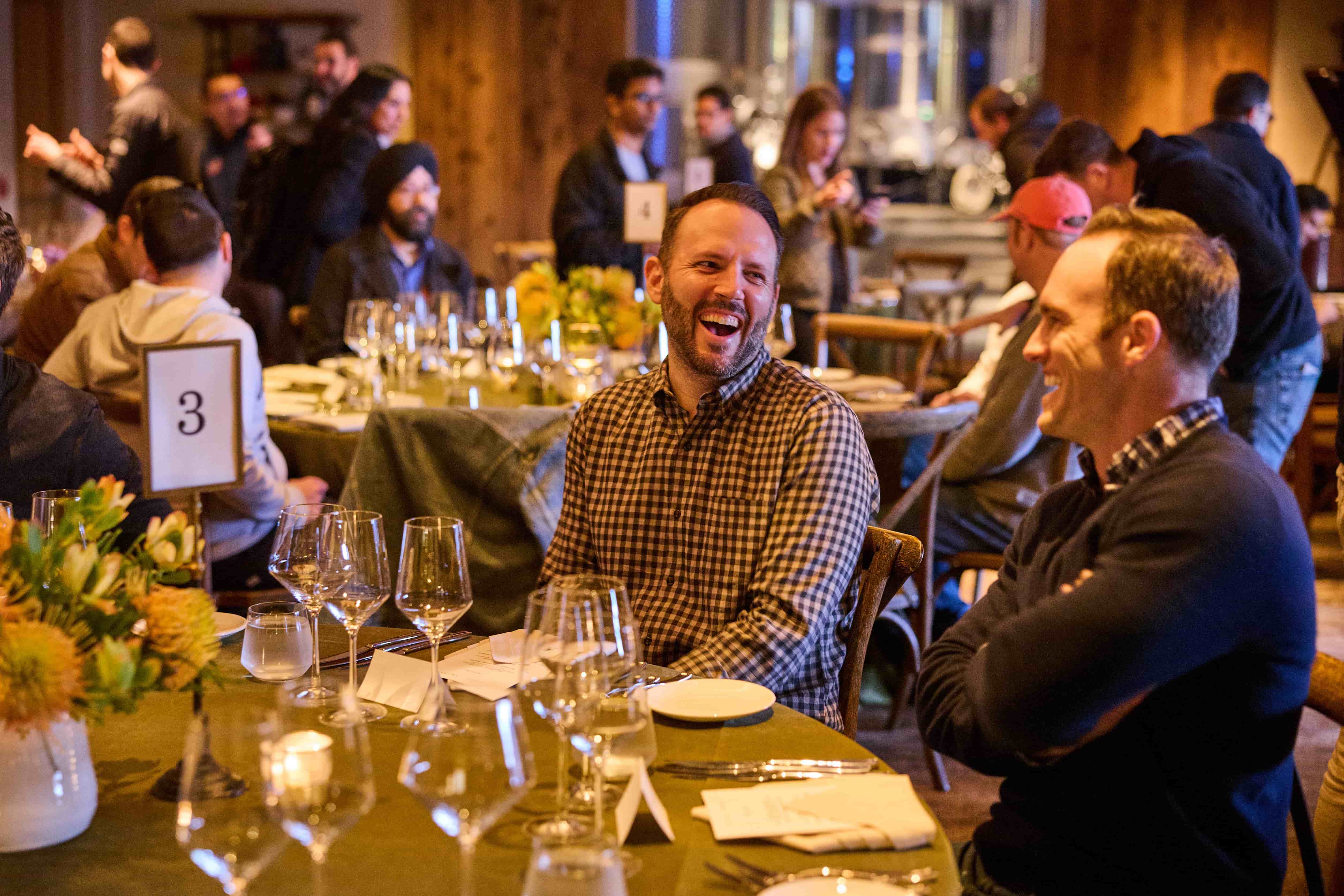 Two professionals in conversation at a dinner table with warm lighting and glasses on the table