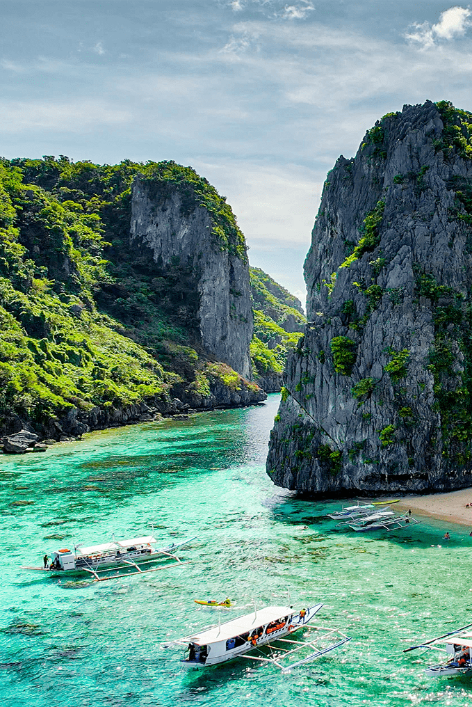 Photograph of a lagoon in the Philippines with bright clear water, a group of boats, white sand beach, and limestone cliffs