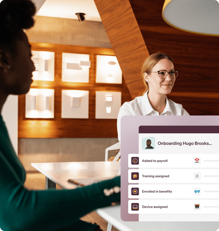 Screen showing an employee onboarding checklist with steps including "Added to payroll," "Training assigned," "Enrolled in benefits," "Device assigned," overlaid on top of a photograph of two employees at a conference room table