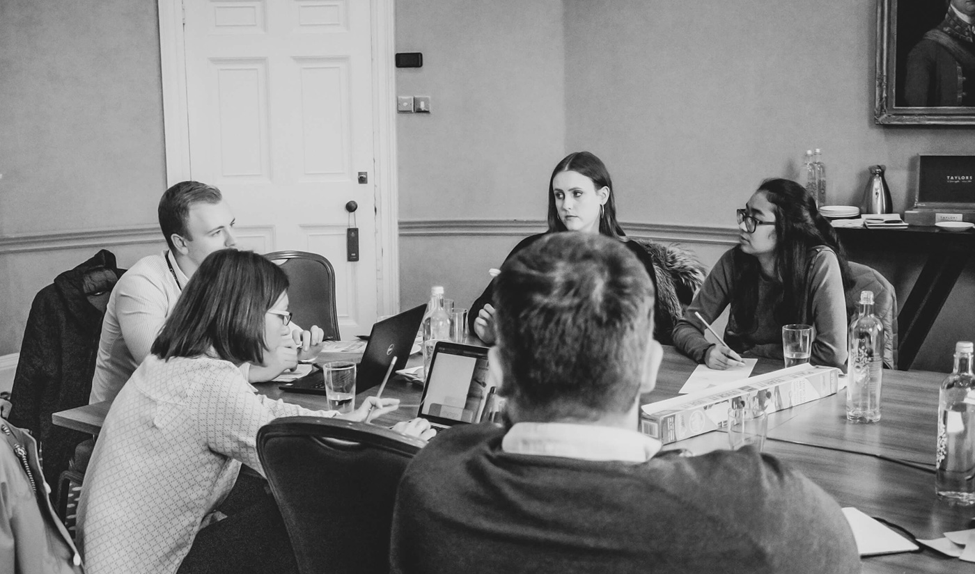 People sat around a table with notepads and laptops open during a UX design sprint