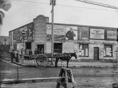 The façade of Thomas Skelly’s produce store on the corner of Missenden and Parramatta roads in 1912. This view shows men and woman on the pavement in front of the store, a lamp post and horse drawn cart. City of Sydney Archives A-01000368.