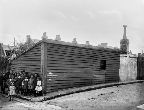 A group of children pose in front of a ramshackle timber outbuilding on the corner of Sutton and Bourke lanes, at the rear of 170–172 Palmer Street, Darlinghurst in 1917. In the 1990s, buildings and streets here were obliterated to make way for the Eastern Distributor. City of Sydney Archives A-01000427.