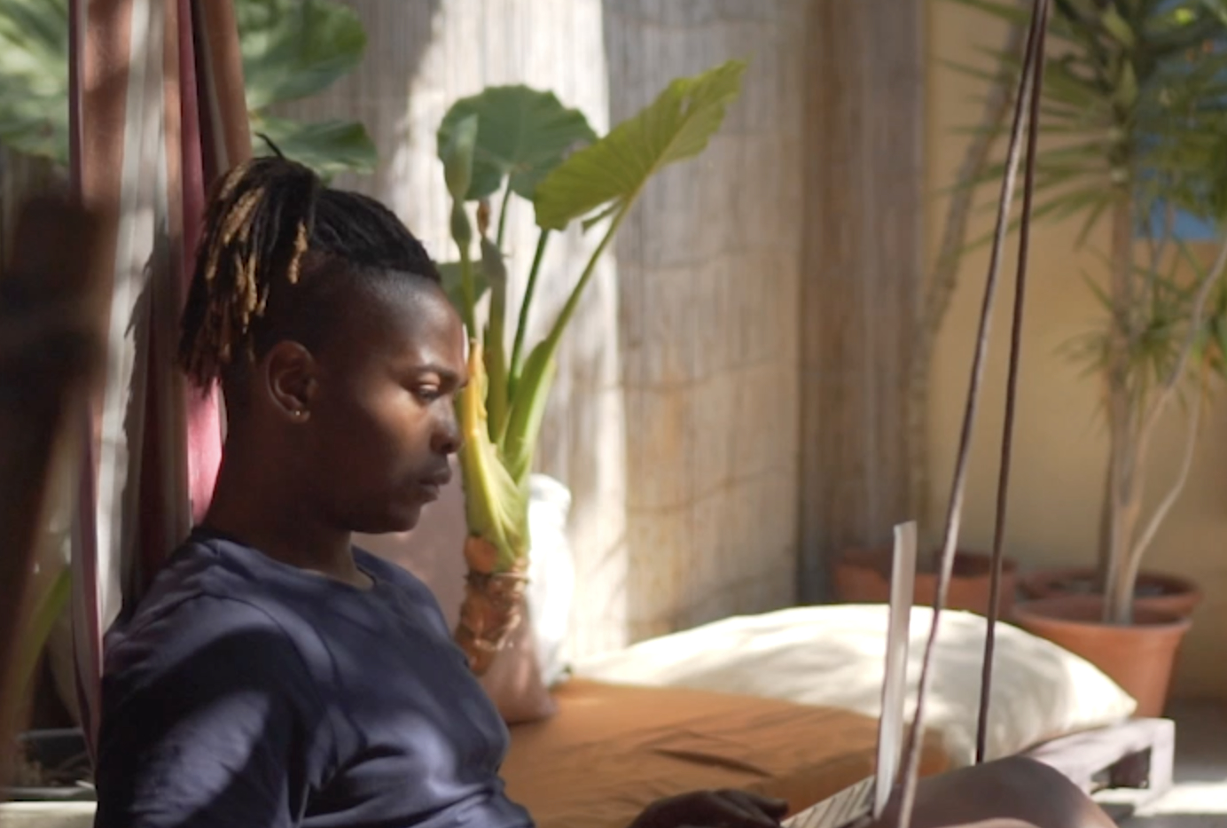 Schwarzer männlicher digitaler Nomade, freiberuflich, auf einer Hängematte, arbeitet mit einem Laptop"