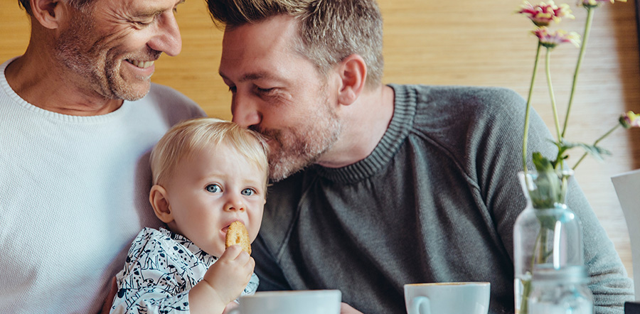Baby krijgt een kusje op zijn hoofd van zijn vader aan de ontbijttafel. 