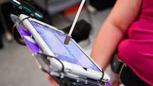 A woman wears an long skinny instrument with a soft tip to push the keyboard buttons on her smart tablet to compose an email.