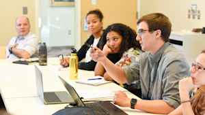 A male CU student holds his pen in his hand to make a point during a group discussion about the asthma study as Fernando Holguin, MD, looks on.
