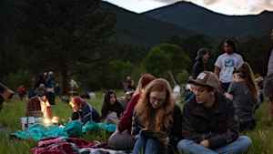 College students sit on blankets on the ground as dusk settles in along the flatirons. They are on a field trip, taking notes by lantern and lamp about the night sky.