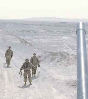Three US Army soldiers walk along a barren desert road in Afghanistan scanning the ground for IEDs
