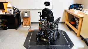 Designed by a student, a test wheelchair sits idle on a solar charging pad.