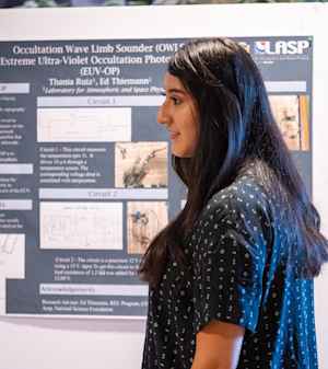 A female CU student with long dark hair and a blue shirt explains her research poster at an expo on the CU Boulder East Campus.
