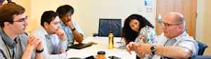 A male physician speaks at a conference table where CU researchers and students sit to discuss a research project.