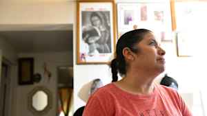 A mother listens in her living room to CU students and researchers as they explain the research project. A picture of the Virgin Mary hangs behind her on the wall.