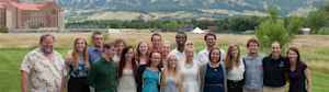 A large group of space science students stand on East Campus of CU Boulder with the majestic Flatirons behind them.
