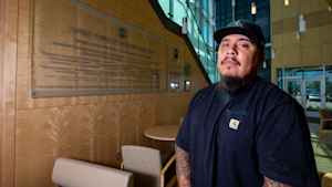 Mike, a US Army veteran, wears a goatee and moustache, a black sports cap and black T-shirt, while standing in the lobby of the Lane Center where he receives mental health care for trauma experienced in combat.