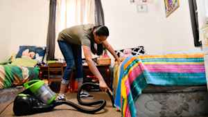 A teenage girl bends over to vacuum the carpet in her bedroom that she shares with her sister