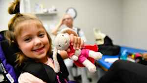 A young girl holds up to show off her beloved stuffed toy, a faded pink bunny, and smiles.