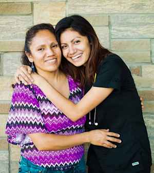 A CU medical student in her scrubs and with a stethoscope smiles and embraces her mother