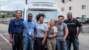 A group of CU students and researchers smile and stand in front of a van with community organizers before they begin their street outreach in Aurora, Colorado.