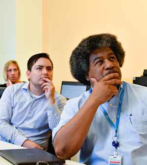 Two men, a student and a community health expert, listen with their hands to their mouths during a meeting about the research project.
