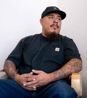 Mike, a US veteran, sits in a chair with his hands folded together as he tells his stories of combat
