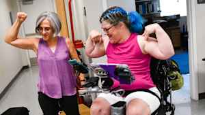 A clinic coordinator and woman in a wheelchair both flex their forearms triumphantly and smile.