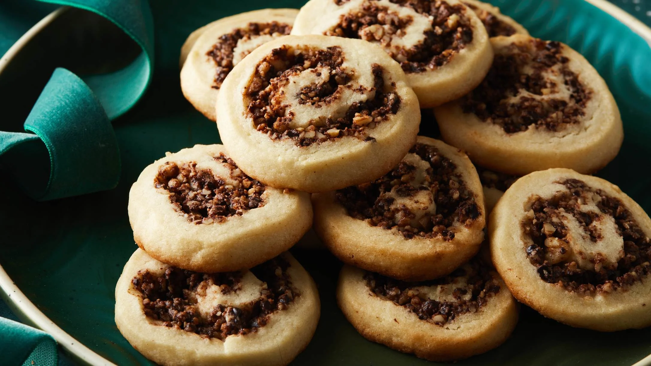 Freshly baked pinwheel cookies with chocolate and nut filling stacked on a teal green plate.