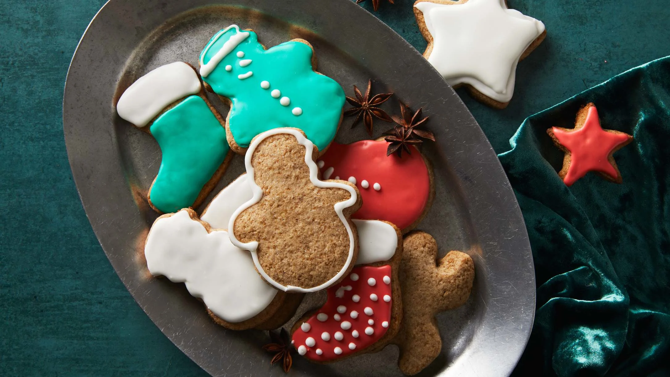 Festive Christmas cookies with icing in teal, red, and white shapes including stockings, stars, and gingerbread men on a metal plate.