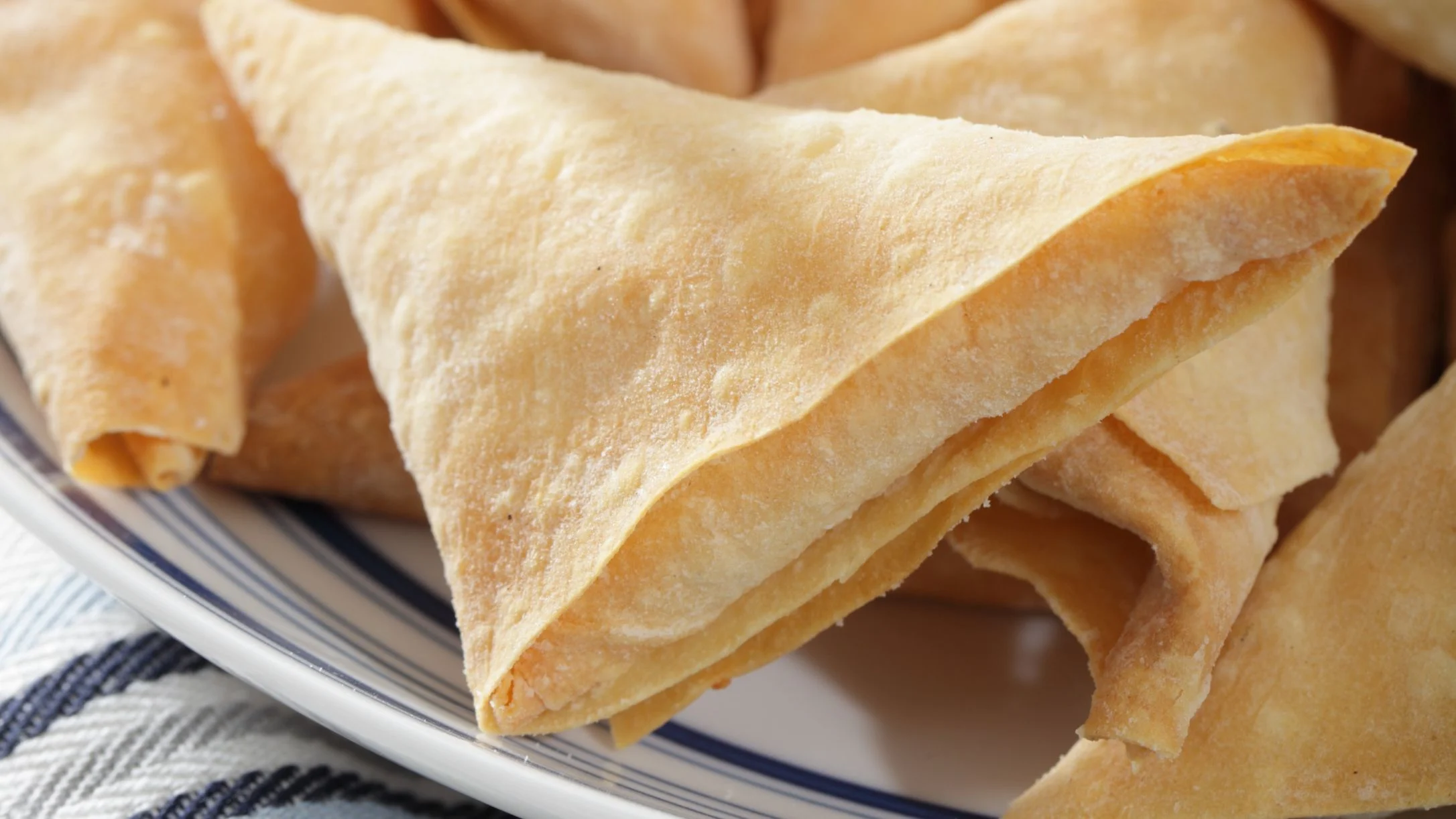 Golden, folded crepes stacked on a white plate with blue trim, placed on a blue and white striped cloth.