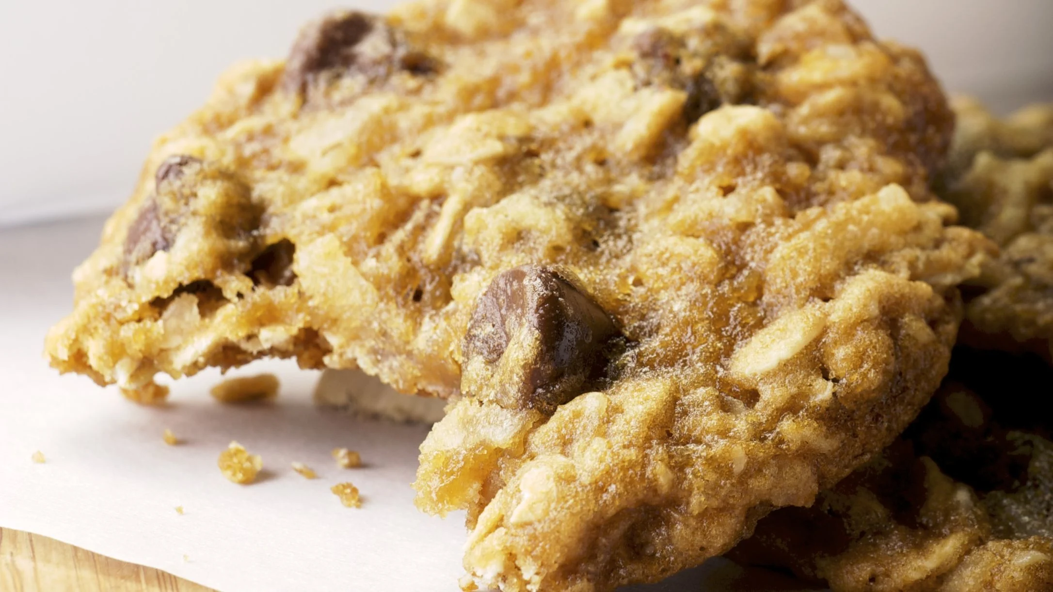 Close-up of a golden-brown oatmeal chocolate chip cookie broken in half, showing a chewy texture with visible chocolate chips.