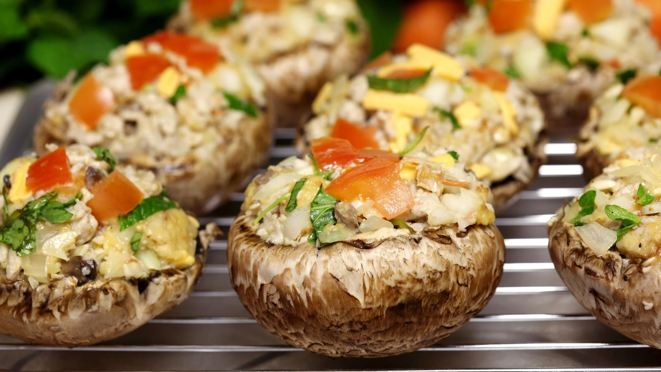 Stuffed mushrooms on a baking rack, filled with diced tomatoes, cheese, herbs, and a savory mixture.