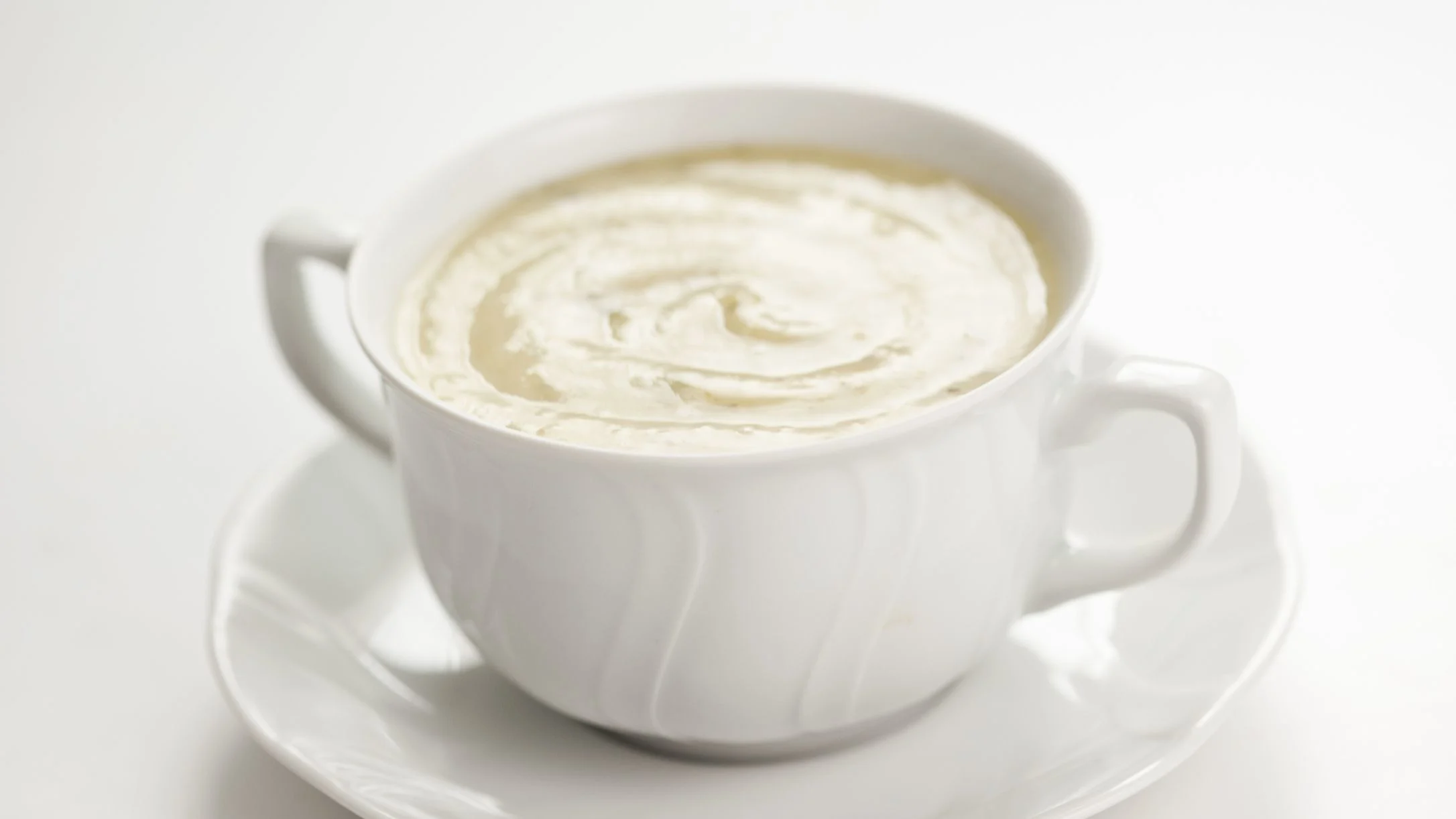 A white ceramic cup on a saucer filled with a creamy swirled dip, on a white background.