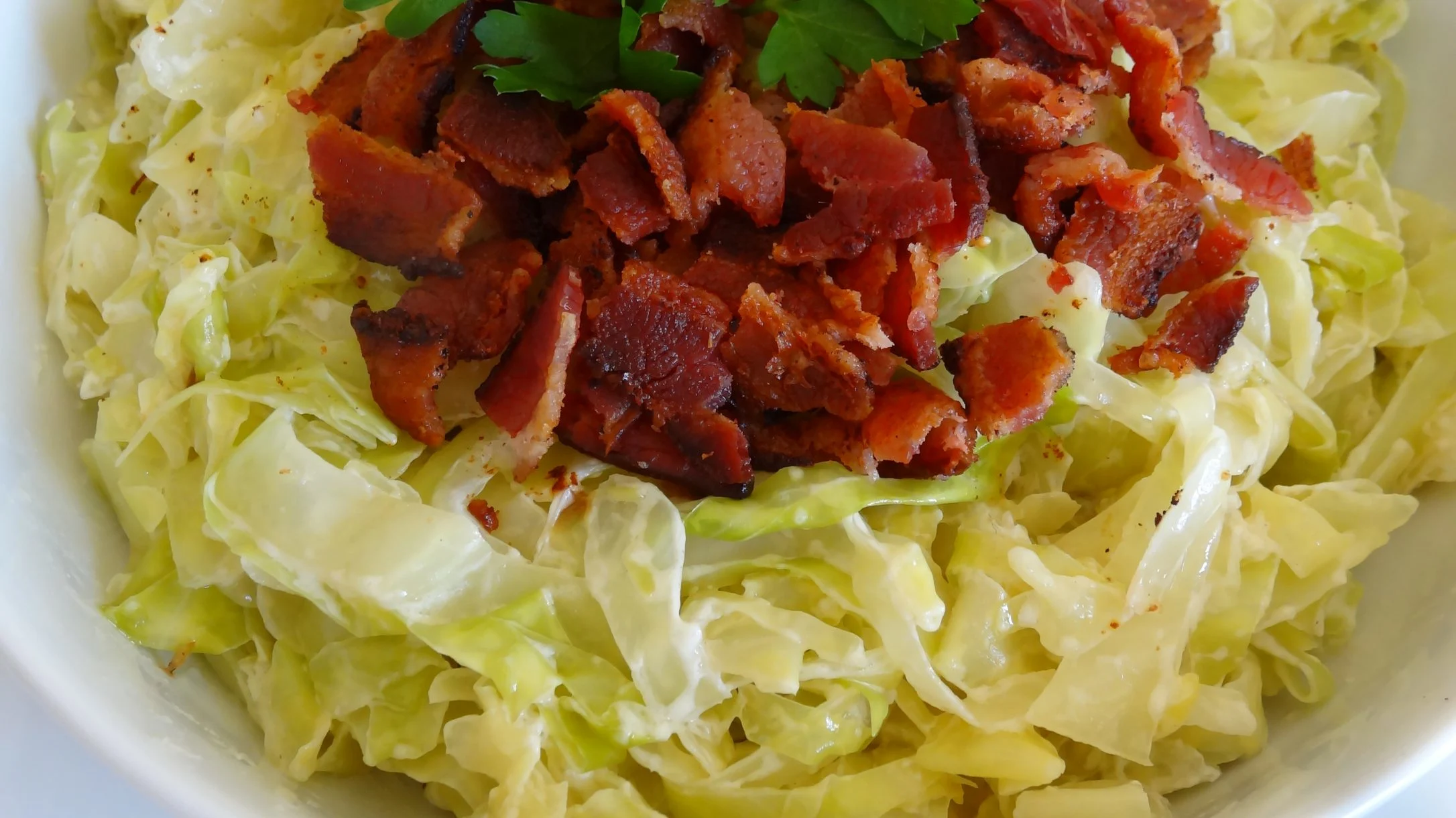 Crispy bacon bits on shredded cabbage in a white bowl, garnished with fresh parsley.