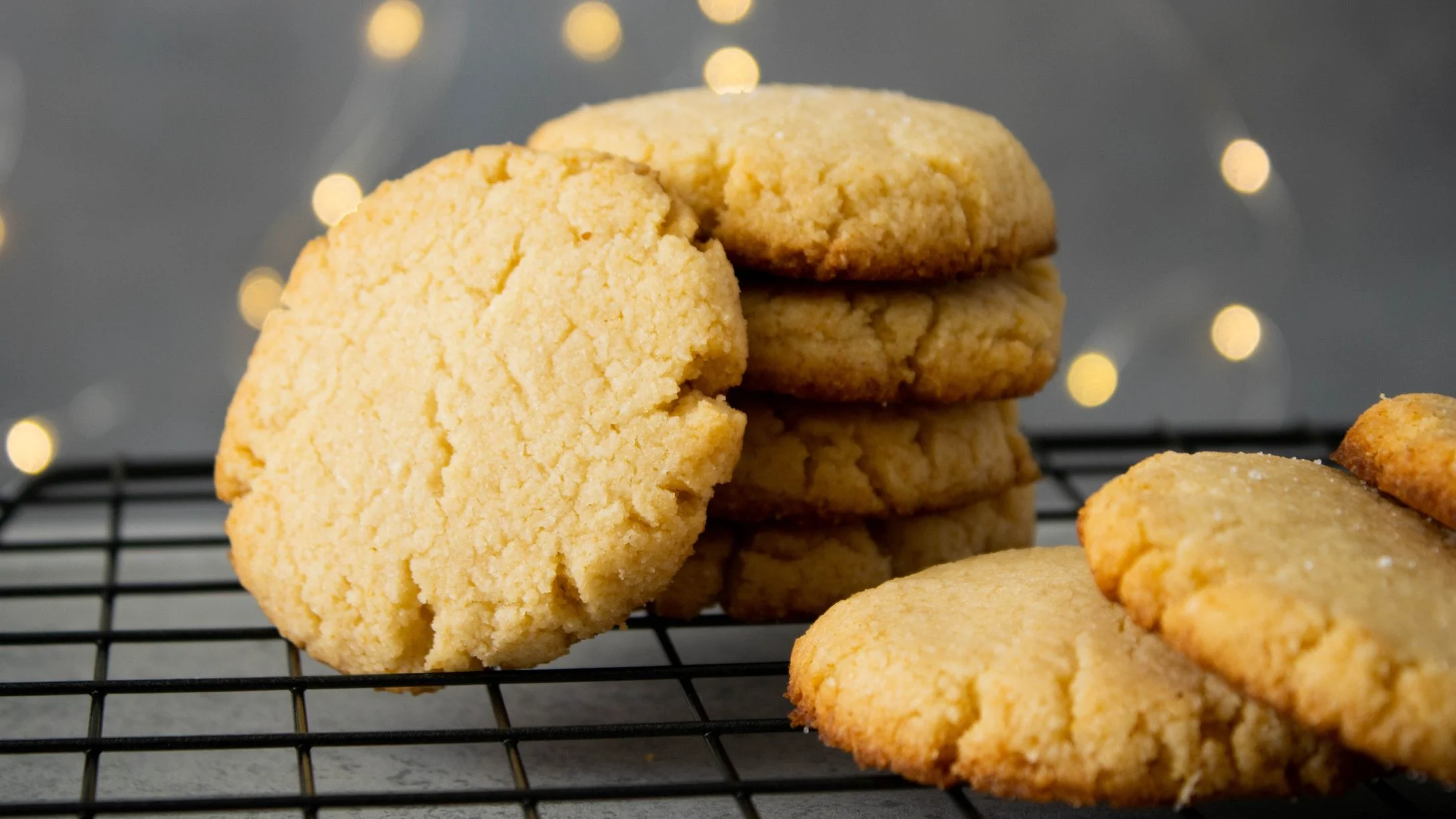 Golden cookies stacked on a cooling rack with soft bokeh lights in the background.