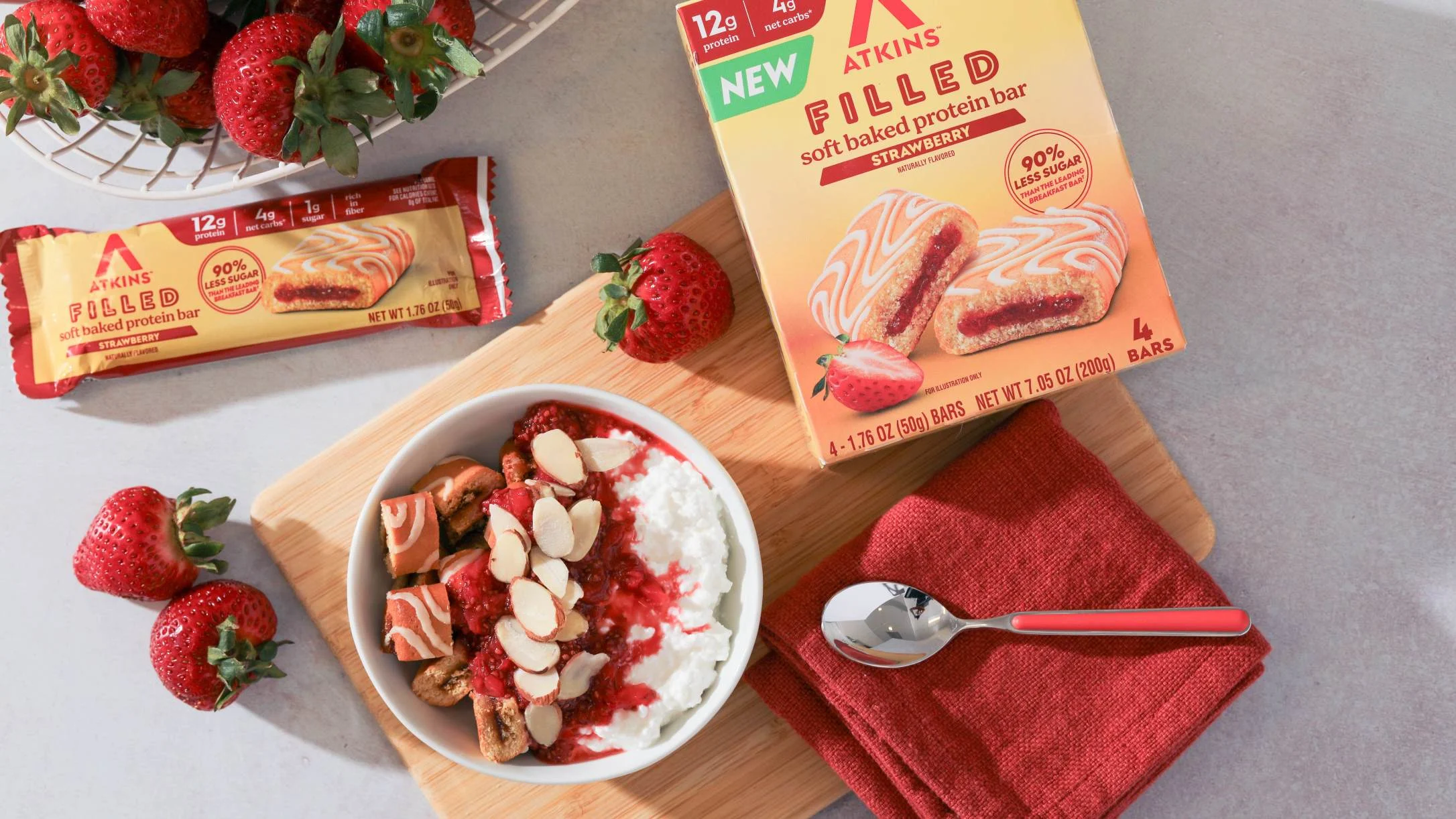 Atkins Filled Strawberry Soft Baked Protein Bar box and wrapper beside a cottage cheese bowl with strawberries and almonds.