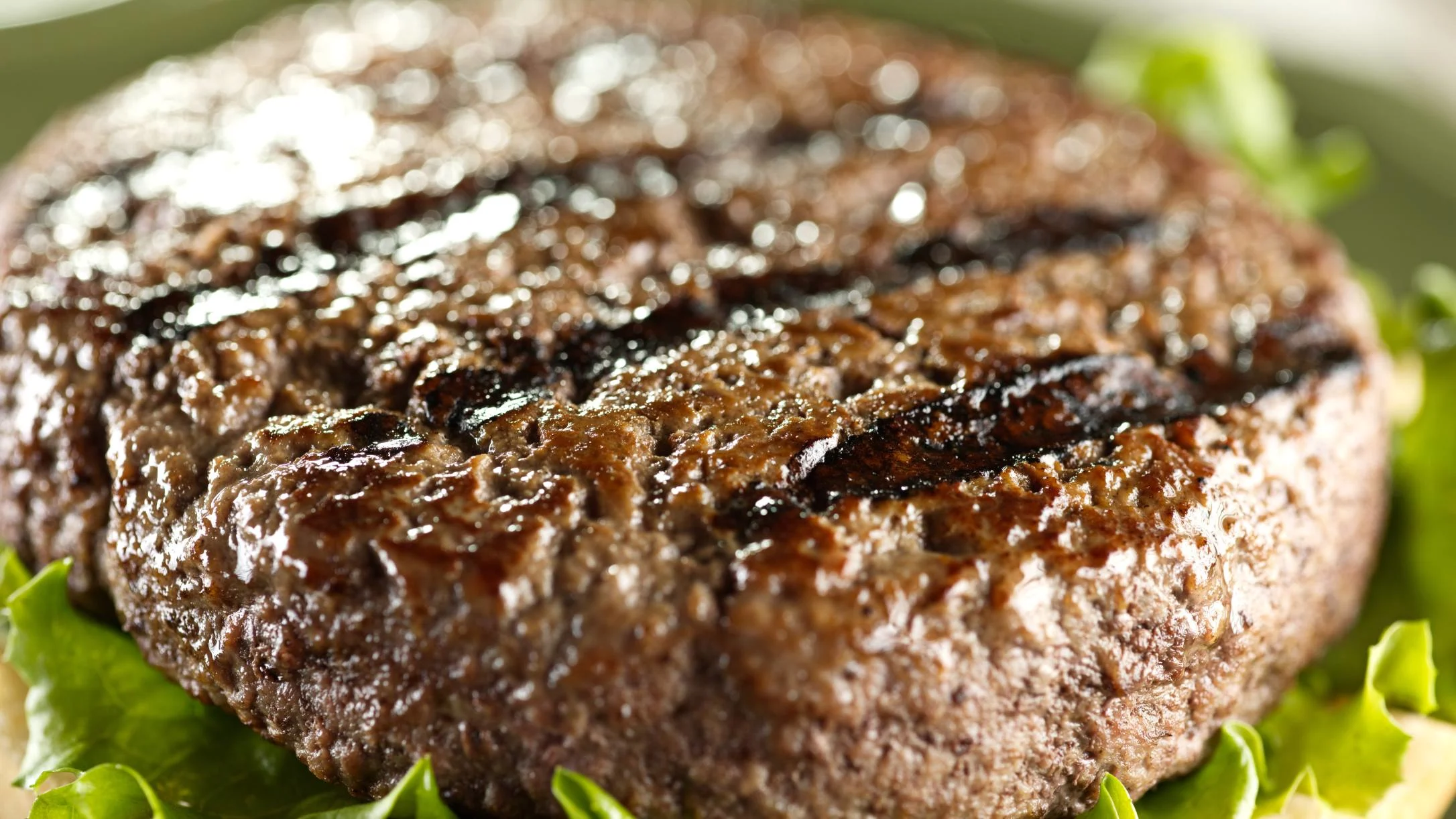 Juicy grilled beef burger patty with grill marks on a bed of fresh green lettuce, close-up view.