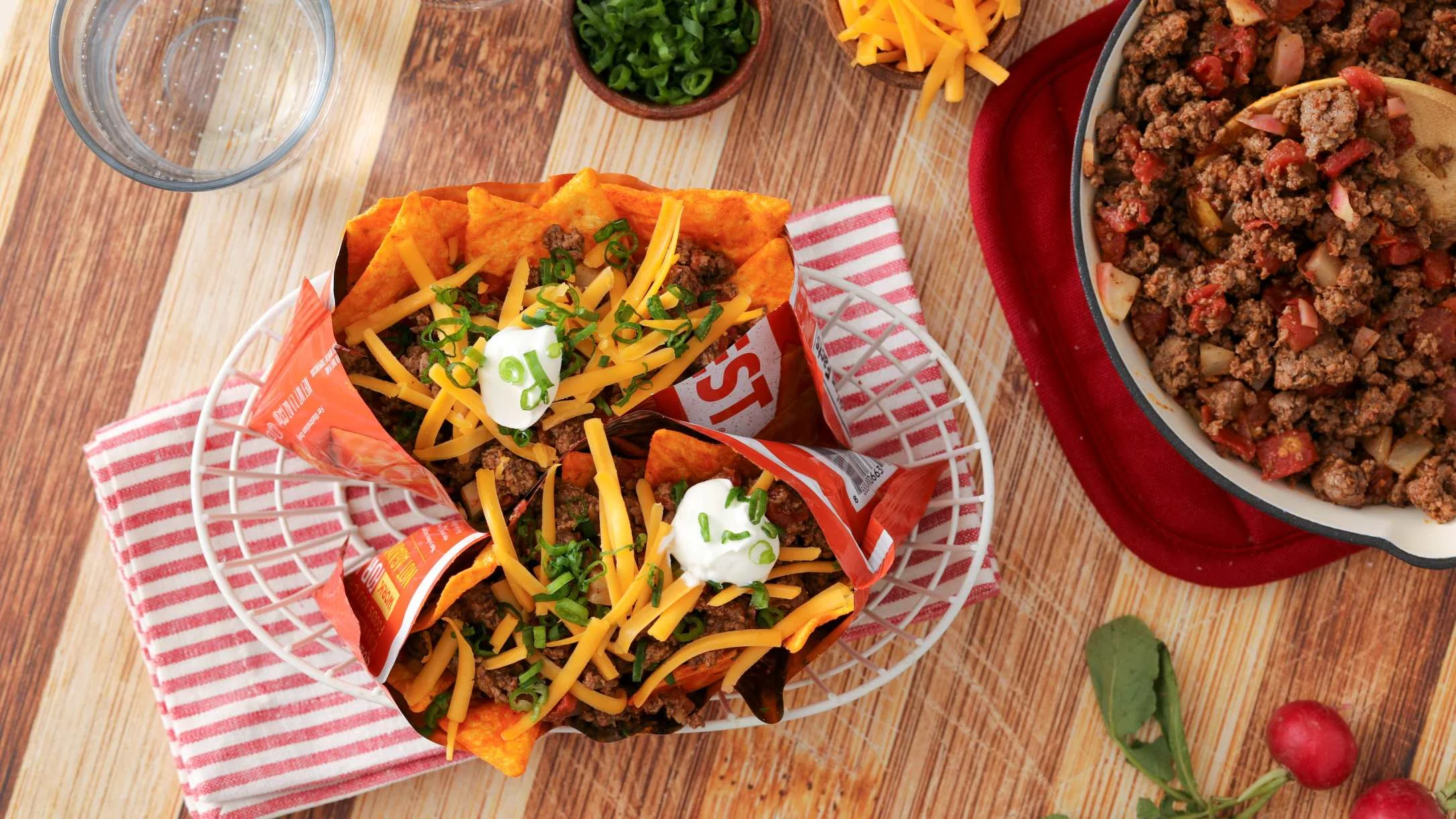 Walking taco bags filled with seasoned ground beef, cheese, and sour cream, served with a pan of taco meat nearby.