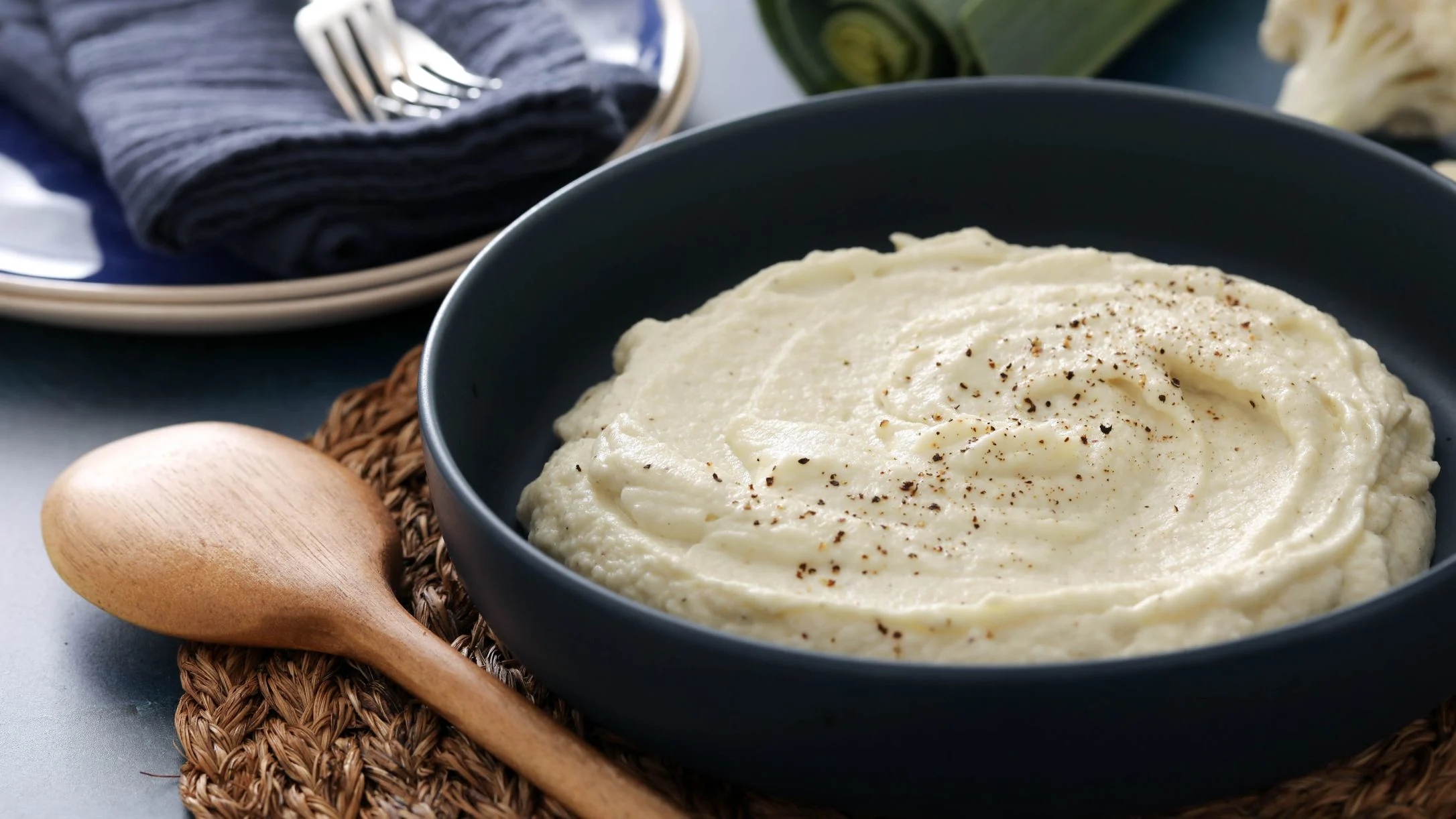 Puree of cauliflower in a blue bowl with a wood spoon and blue plates near.