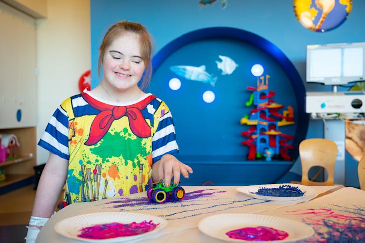 A girl in the hospital with a starlight hospital gown on playing with toys and paint