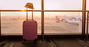 Försenat eller förlorat bagage Rosa resväska vid gaten med utsikt över flygplanen.