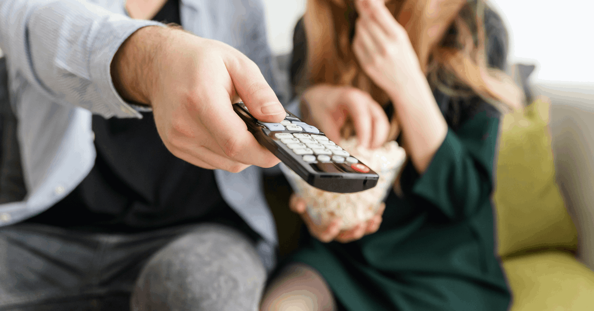 svenska-elnotan-vm-2022.png Par som sitter i en grön soffa hållandes i popcorn och fjärrkontroll.