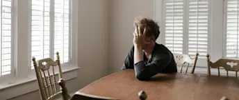 BRF Konkurs Man med huvudet i handen sittande vid ett matbord med neddragna persienner för fönstren.