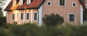Hus med grönt bolån Äldre hus med vita knutar och rosa puts, omgiven av gröna buskar