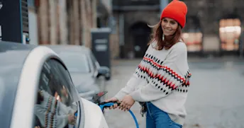 laddhybrid Kvinna i stickad tröja och orange mössa laddar en hybridbil.