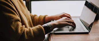 Distansarbete Närbild av kvinna i senapsgul stickad tröja som arbetar på sin bärbara dator