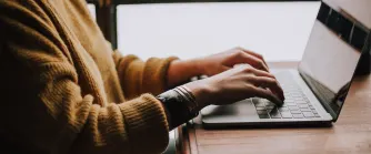 Närbild av kvinna i senapsgul stickad tröja som arbetar på sin bärbara dator