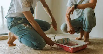 renovera hem kvinna och man i blåa jeans och vita t-shirtar sitter på knä framför ett tråg med målarfärg.